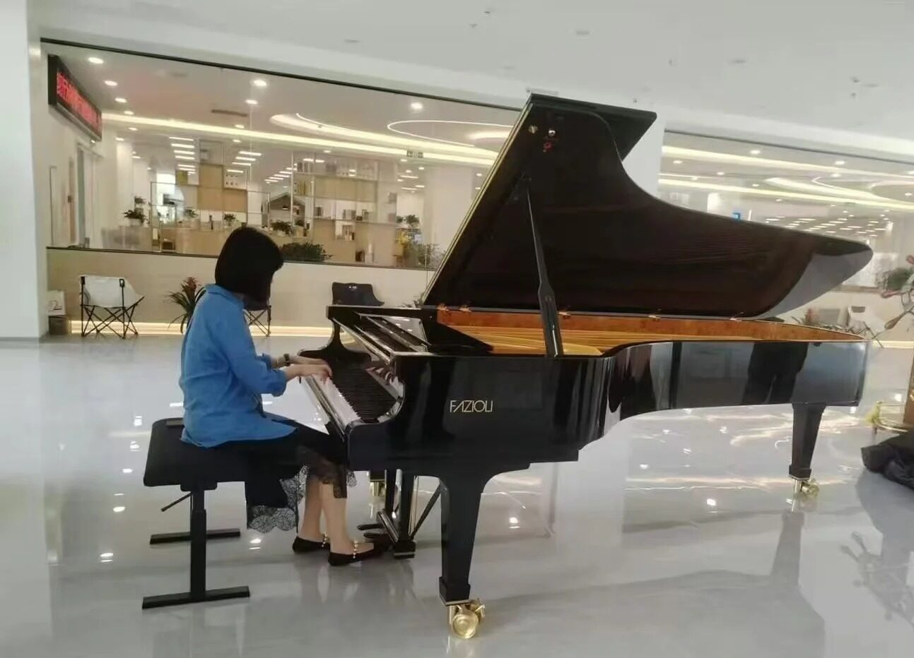 Pianistka w niebieskiej bluzce grająca na czarnym fortepianie w nowoczesnej sali