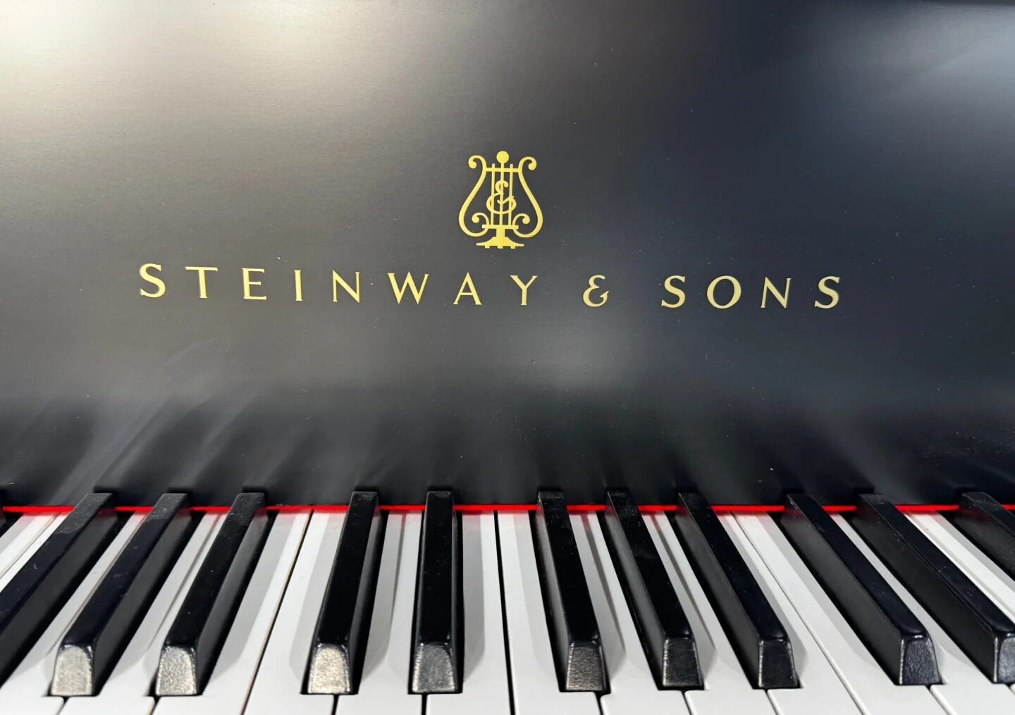Klawisze fortepianu Steinway & Sons z widocznym złotym logiem marki nad nimi