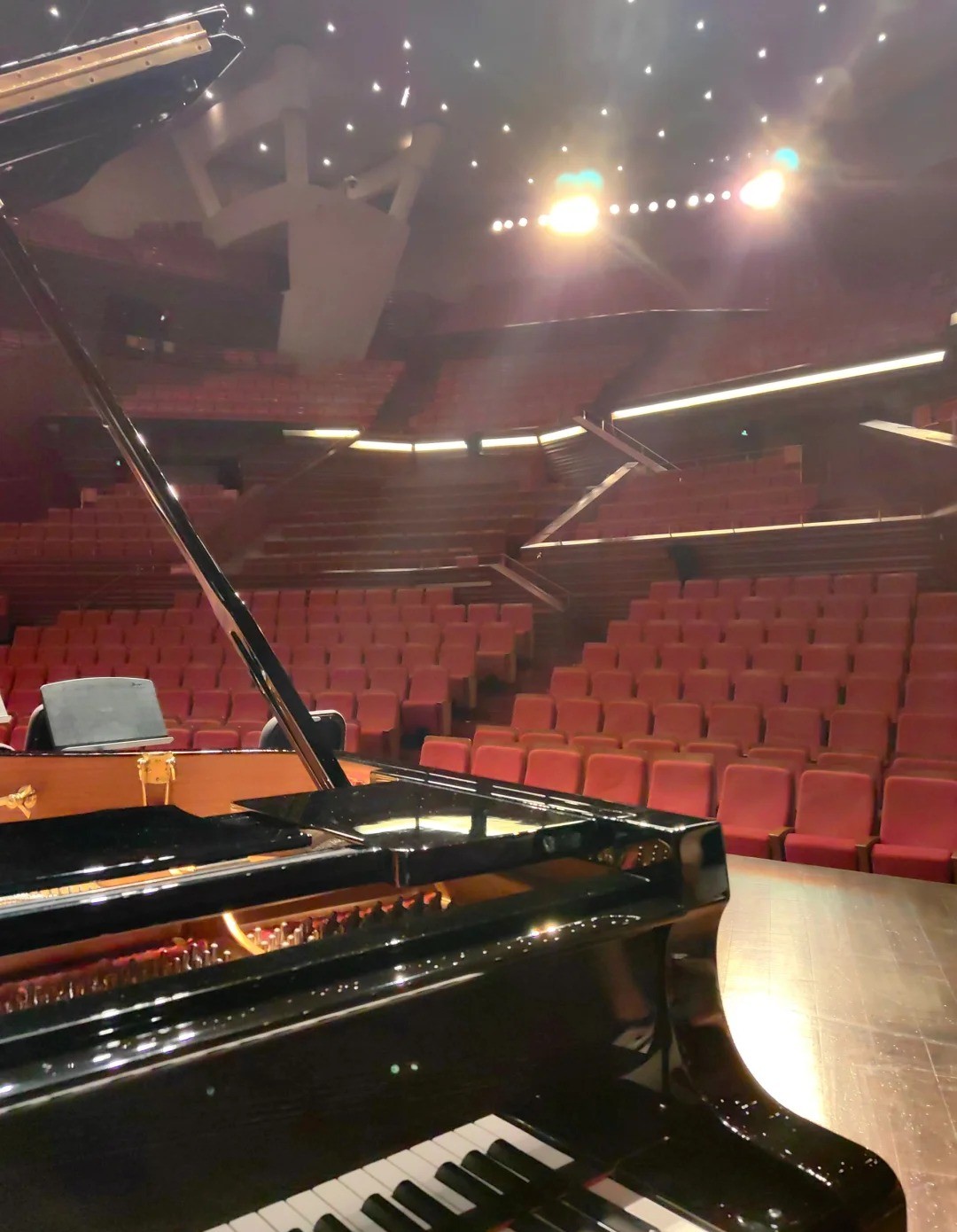 Piano à queue pour concert sur scène dans une salle avec fauteuils rouges et éclairage de spectacle
